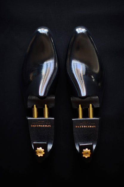 Pair of black shoe trees with gold accents on a dark background