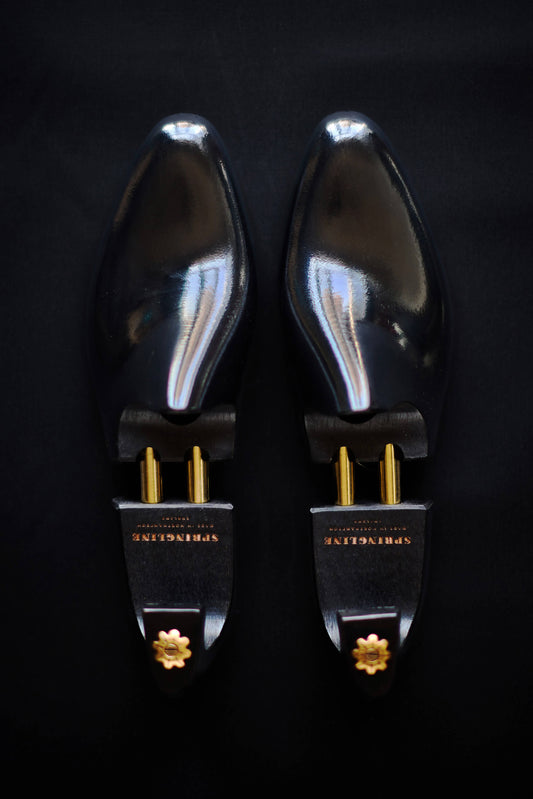 Pair of black shoe trees with gold accents on a dark background