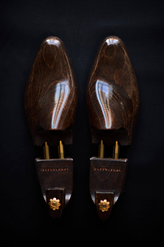 A pair of brown wooden shoe trees with metal hardware against a dark background.