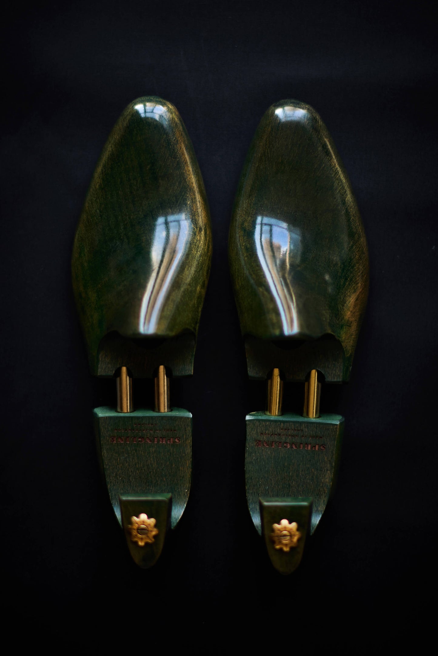 A pair of green shoe trees with gold accents on a dark background.