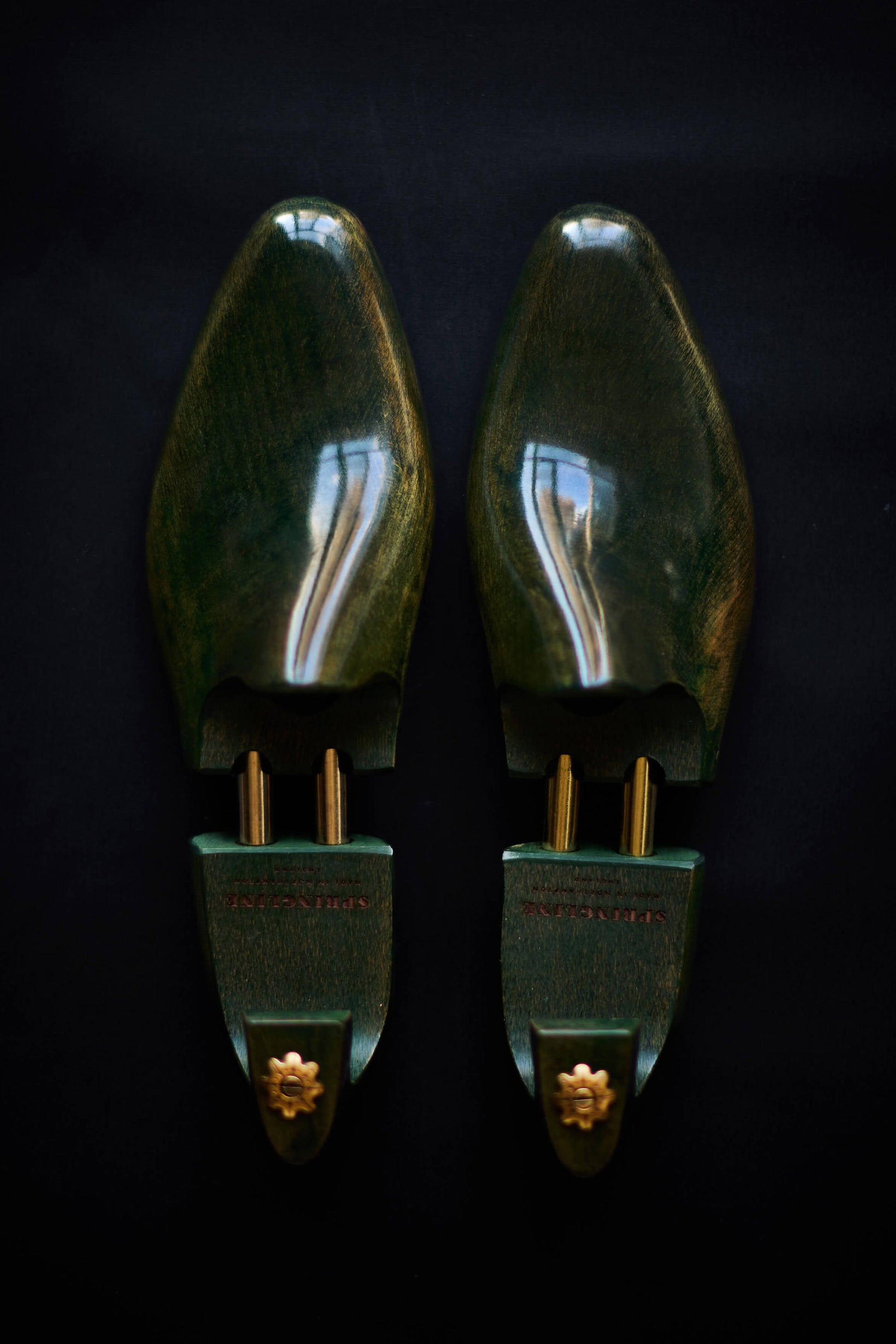 A pair of green shoe trees with gold accents on a dark background.