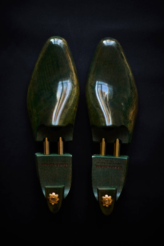 A pair of green shoe trees with gold accents on a dark background.