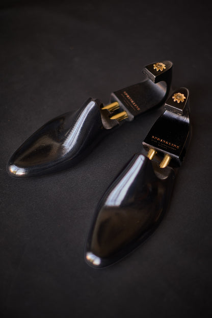 Pair of black shoe trees with gold accents on a dark background