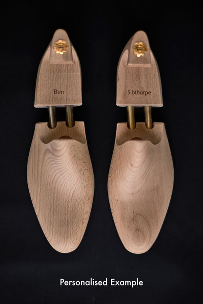 Pair of wooden shoe trees with personalised name on a black background.