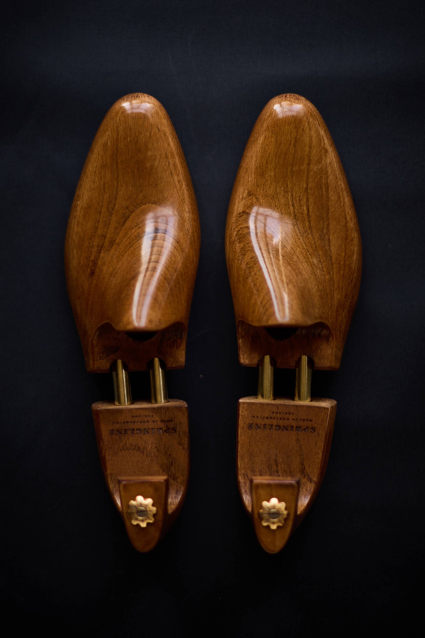 A pair of brown wooden shoe trees with metal hinges displayed against a dark background.