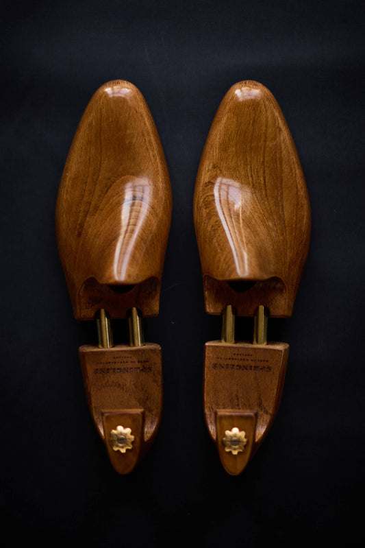 A pair of brown wooden shoe trees with metal hinges displayed against a dark background.